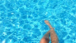 jambes de femme trempant dans l'eau bleue d'une piscine