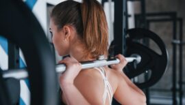 femme se préparant à faire du squat à la barre libre sollicitant les trapèzes