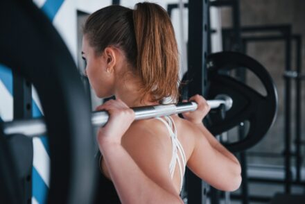 femme se préparant à faire du squat à la barre libre sollicitant les trapèzes