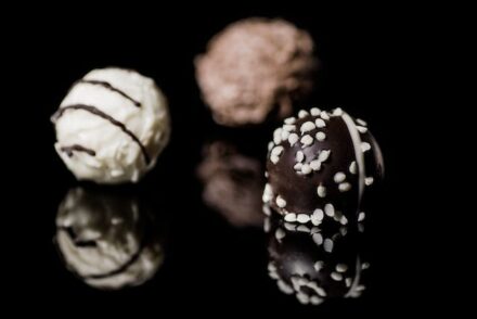 3 chocolats de Noël (noir, blanc et au lait) posés sur une surface noire laquée