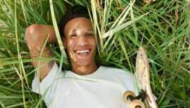 homme de couleur souriant couché sur l'herbe avec son skate à la main