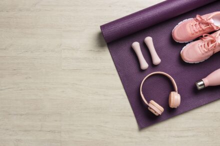 haltères, casque de sport, gourde et baskets roses sur un tapis de fitness violet