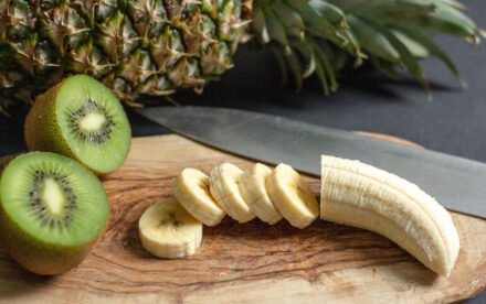banane coupée en rondelles et kiwi coupé en deux avec un ananas en arrière plan